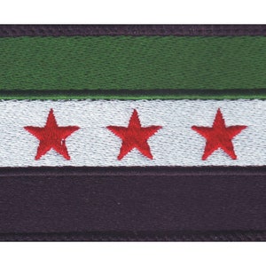 May include: Embroidered patch featuring the flag of Syria. The design includes a green stripe at the top, a white stripe with three red stars in the center, and a black stripe at the bottom. The patch has a black border.
