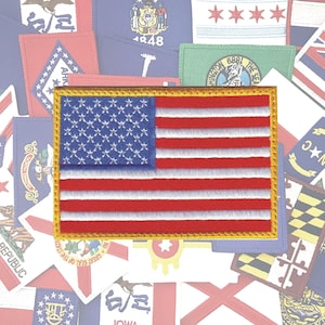 May include: A close-up of an embroidered American flag patch with a gold border. The flag is red, white, and blue with 13 stripes and 50 stars.