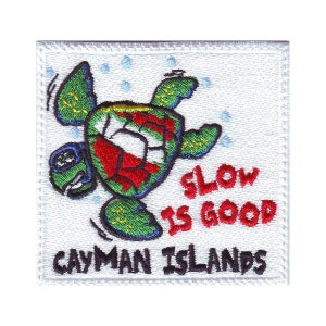 May include: A white embroidered patch with a cartoon sea turtle swimming with the text "Slow is good" and "Cayman Islands" below.