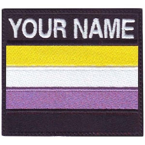 May include: A black and white embroidered patch with the text "YOUR NAME" above a yellow, white, and purple striped flag. The flag is a symbol of non-binary pride.