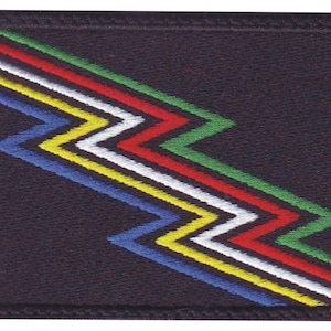 May include: A rectangular patch with a dark navy blue background. A zig-zag design in blue, yellow, white, red, and green is embroidered across the patch. The patch has a black border.