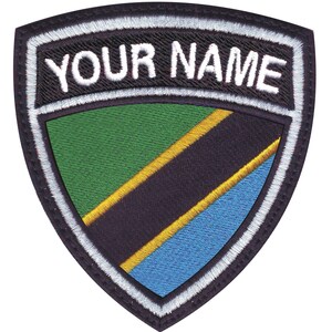 May include: Embroidered patch in a shield shape, featuring the text "YOUR NAME" above a design with green, black, yellow, and blue stripes, resembling a flag. The patch has a black border with white stitching.