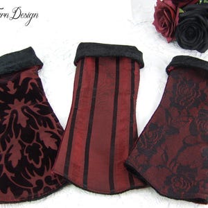 Könnte beinhalten: Drei rote und schwarze Stoff-Handgelenksmanschetten mit verschiedenen Mustern. Die Manschetten haben einen schwarzen Samtbesatz. Die Muster umfassen ein Damastmuster, vertikale Streifen und ein Blumenmuster.