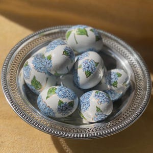 May include: A silver bowl filled with white eggs decorated with blue and green hydrangea flowers.