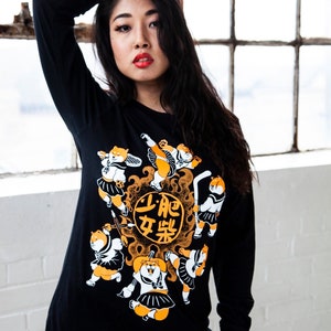 May include: Black long-sleeved shirt featuring a graphic print of cartoon dogs wearing school uniforms and playing sports. The text "上吧 女将" is printed on the shirt.