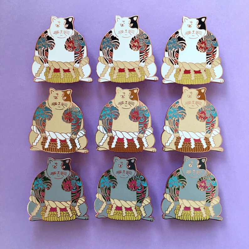 May include: Nine enamel pins featuring cats dressed as sumo wrestlers. The cats are wearing traditional sumo wrestling outfits with colorful designs and are in various poses. The pins are a mix of white, black, and gray cats.