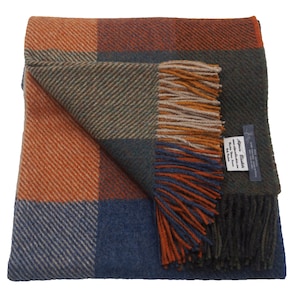May include: A green, blue, orange, and brown plaid throw blanket with fringe. The blanket is folded in half and the label "Harris Tweed" is visible.