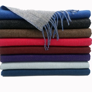 May include: A stack of ten scarves in various colors, including blue, gray, brown, red, burgundy, purple, light blue, and dark blue. The scarves are folded and stacked neatly, with the top scarf folded in half and draped over the stack.