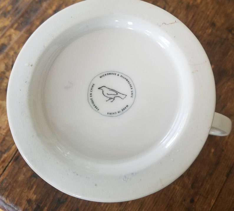 May include: White ceramic mug with a black bird illustration and the text "Microwave & Dishwasher Safe. Made in China. Fabriqu&eacute; en Chine" on the bottom.