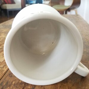 May include: White ceramic mug with a smooth, glossy finish. The mug is empty and has a rounded shape with a handle.
