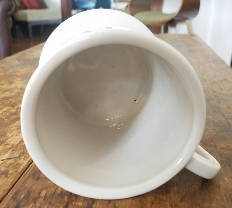 May include: White ceramic mug with a smooth, glossy finish. The mug is empty and has a rounded shape with a handle.