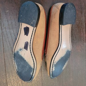 May include: A pair of tan leather loafers with black soles. The loafers have a brown leather trim around the edges.