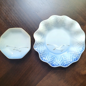 May include: Two porcelain plates with a seagull design. One is octagonal with a gold rim, the other is round with a scalloped edge. Both plates have a light blue and white color scheme with a gold seagull illustration.