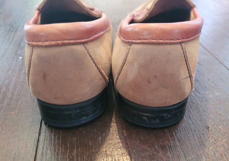 May include: A pair of brown suede leather loafers with a brown leather trim around the top. The loafers have black rubber soles.