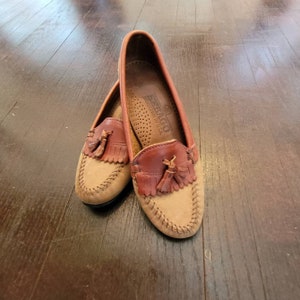 May include: A pair of brown leather tassel loafers with a tan suede toe. The loafers are made by Sebago and are handcrafted in the USA.