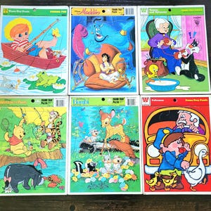 May include: A collection of six vintage frame-tray puzzles featuring colourful cartoon illustrations of characters including Aladdin, Winnie the Pooh, Bambi, Tweety and Sylvester, a child fishing, and a police officer with a school bus.