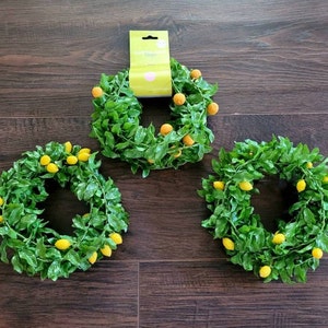 May include: Three green leaf wreaths with yellow lemons. The wreaths are made of artificial leaves and lemons.