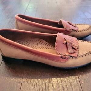 May include: A pair of brown leather loafers with a tassel detail. The loafers have a light brown suede upper and a darker brown leather trim.