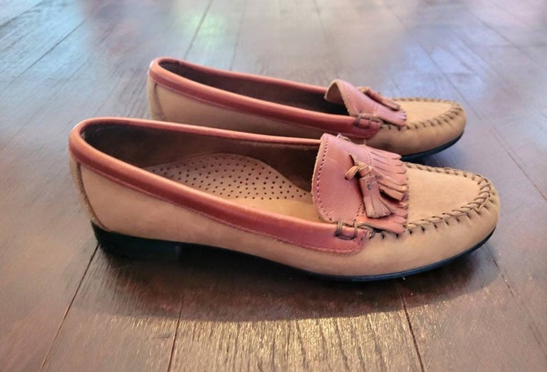 May include: A pair of brown leather loafers with a tassel detail. The loafers have a light brown suede upper and a darker brown leather trim.