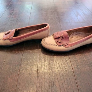 May include: A pair of brown leather loafers with tassels. The loafers have a light brown upper and a darker brown trim around the edges. The tassels are made of the same leather as the loafers.
