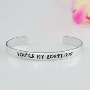May include: Silver bracelet with the inscription "You're my lobster" and a small heart symbol.