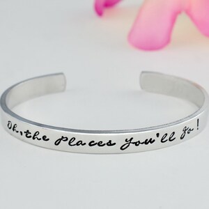 May include: Silver bangle bracelet with the inscription "Oh, the places you'll go!" in black lettering.