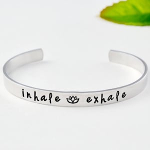 May include: Silver bracelet with the words "inhale" and "exhale" engraved on it, with a lotus flower symbol in between.