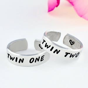May include: Two silver rings with the words "Twin One" and "Twin Two" engraved on them. The rings are stacked on top of each other.