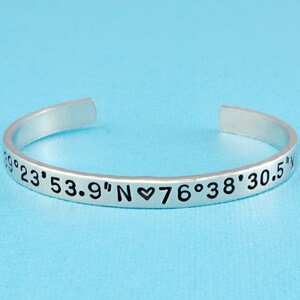 May include: Silver bangle bracelet with the coordinates 23° 53.9" N ♥ 76° 38' 30.5" engraved on it.