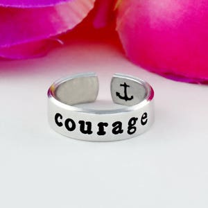 May include: Silver adjustable ring with the word "courage" engraved on the front and an anchor symbol on the back.