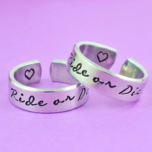 May include: Two silver rings with the inscription "Ride or Die" and a small heart on each ring.