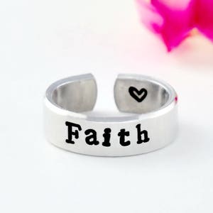 May include: A silver adjustable ring with the word "Faith" engraved on the band. A small heart is engraved on the inside of the ring.