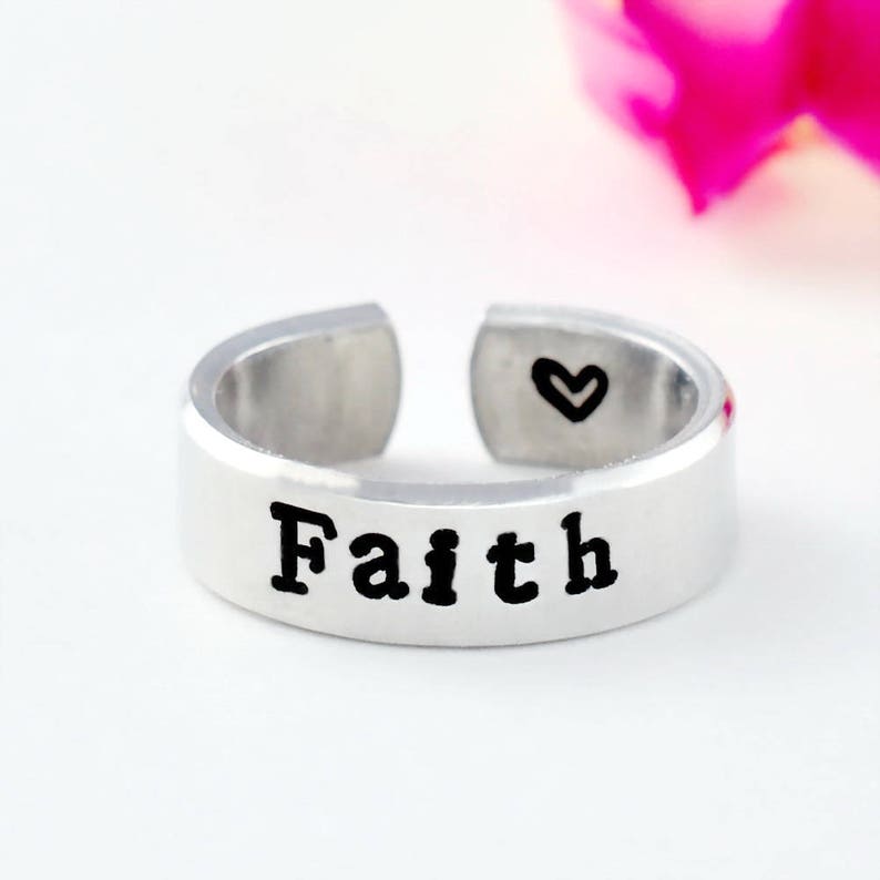 May include: A silver adjustable ring with the word "Faith" engraved on the band. A small heart is engraved on the inside of the ring.