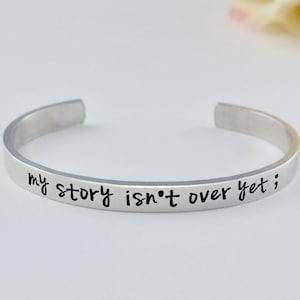 May include: Silver bracelet with the inscription "my story isn't over yet;"