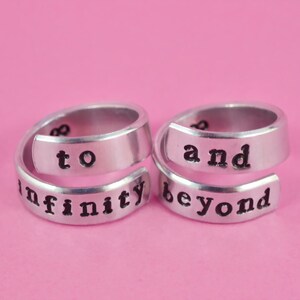 May include: Two silver rings with the words "to infinity and beyond" engraved on them. The rings are designed to be worn together.