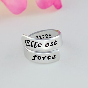 May include: Silver ring with the words "Elle est forte" and the numbers "31:25" engraved on it.