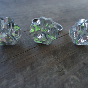 May include: Three silver paw print rings with a clear, textured design. The rings are on a wooden surface.