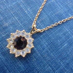 May include: A gold chain necklace with a pendant featuring a black stone surrounded by clear rhinestones.