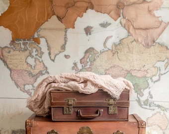 May include: Two vintage brown suitcases with brass hardware and leather handles. The suitcases are stacked on top of each other and are sitting in front of a world map.