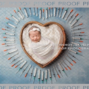 May include: A newborn baby girl is sleeping in a heart-shaped wooden basket surrounded by a circle of syringes on a blue background. The baby is wearing a white swaddle and a white headband with a bow.