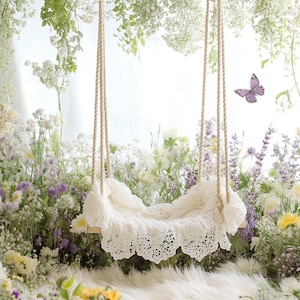 May include: A white crocheted swing with a lace trim hangs in a garden setting with white and purple flowers. The swing is made of rope and has a wooden frame.
