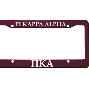 May include: A maroon license plate frame with white lettering. The top of the frame reads "PI KAPPA ALPHA." The bottom of the frame reads "PKA."