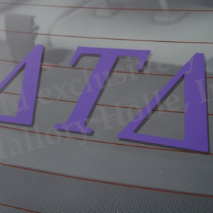 May include: Purple vinyl decal with the letters "ΔΤΔ" on a car window.