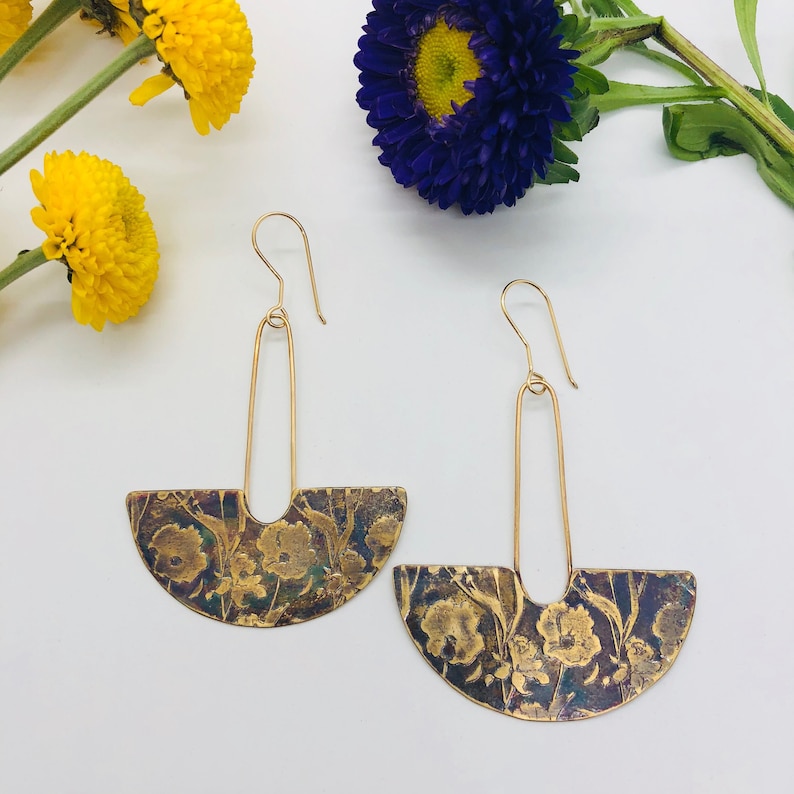 May include: A pair of gold earrings with a floral design. The earrings are made of brass and have a semi-circular shape. The floral design is embossed on the brass and has a vintage look.