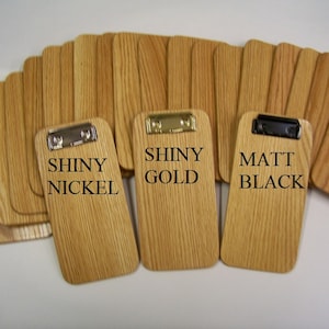 May include: Three wooden clipboards with different colored metal clips. The clipboards are labeled "Shiny Nickel", "Shiny Gold", and "Matt Black".