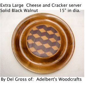 May include: A large, round, wooden cheese and cracker server made of solid black walnut. The server has a decorative inlay of geometric shapes in shades of brown and black. The server is 15 inches in diameter.