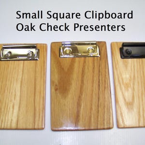 May include: Three small square oak clipboards with the text Small Square Clipboard Oak Check Presenters. Two clipboards feature shiny silver metal clips, while the third clipboard on the right has a matte black metal clip for holding papers.