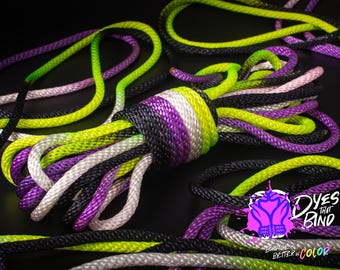 May include: A close-up of a multi-colored rope with black, white, purple, and green stripes. The rope is coiled and tied in a knot. The text "Dyes That Bind" is visible in the lower right corner of the image.
