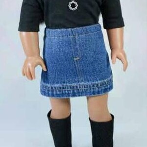 Puede incluir: Una mu&ntilde;eca con una camisa negra de manga larga, una falda vaquera y botas negras. La mu&ntilde;eca lleva un collar de plata con un colgante circular.
