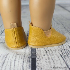 Puede incluir: Un par de zapatos amarillos de cuero para una mu&ntilde;eca. Los zapatos tienen una parte superior de cuero texturizado y una suela marr&oacute;n claro.